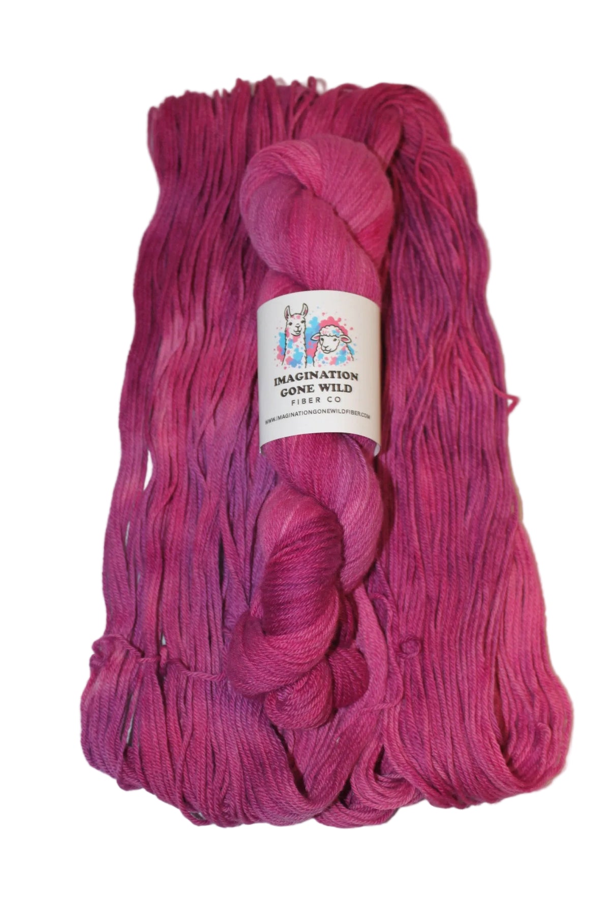 A skein of vibrant magenta and pink ombre yarn with a white paper label, displayed on a neutral light gray background.