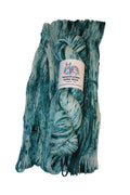 A skein of variegated yarn in shades of teal, blue, and white, with a white paper label wrapped around the center, set against a plain light background.